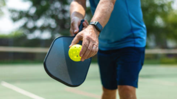 Man dressed in blue holding a pickleball paddle and yellow pickleball